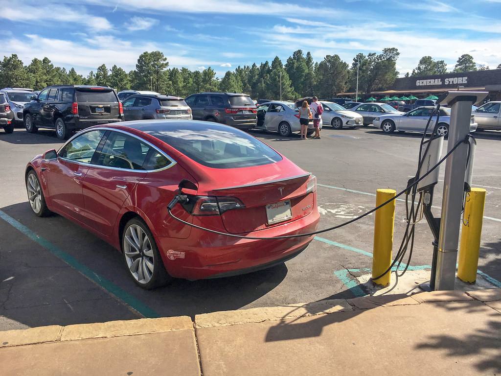 Červená Tesla Model 3 připojená kabelem k nabíjecímu stojanu na parkovišti
