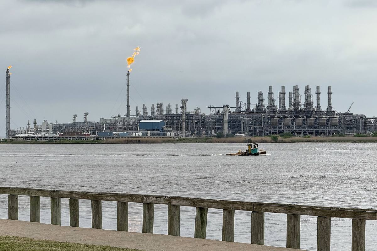 Zkapalňovací terminál Sabine Pass s hořícími fléry, v popředí řeka a remorkér