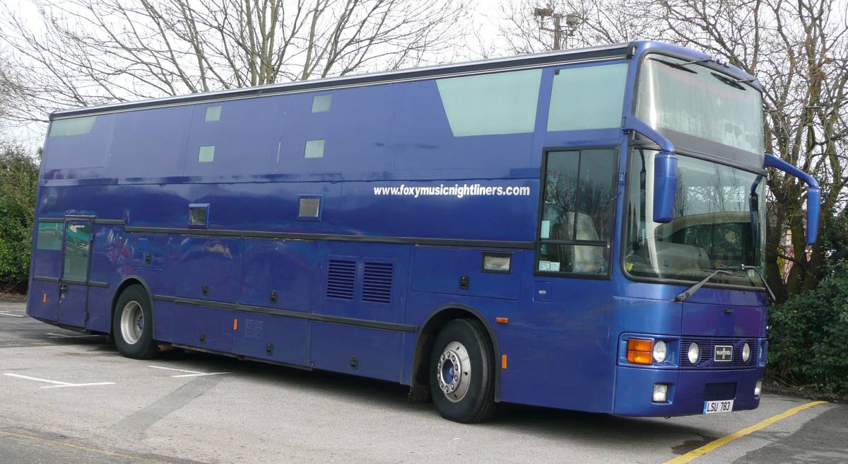 Tmavě modrý nightliner s převážně zaslepenými okny stojí na parkovišti