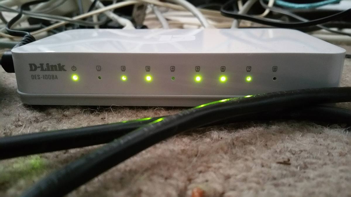 Bílý osmiportový přepínač D-Link se svítícími zelenými kontrolkami a síťovými kabely