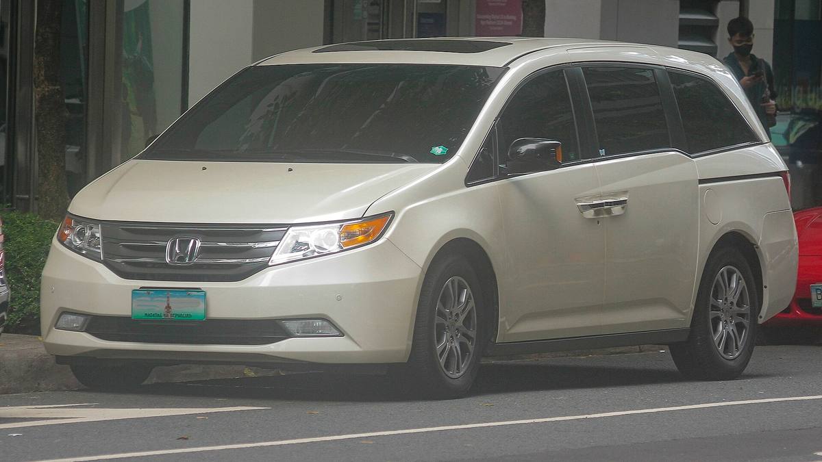 Bílá Honda Odyssey čtvrté generace zaparkovaná u chodníku, pohled zepředu zleva